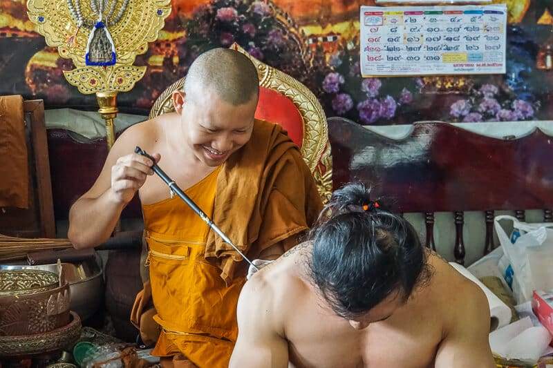 A master monk applying a Sak Yant tattoo by hand during the guided holiday service in Thailand